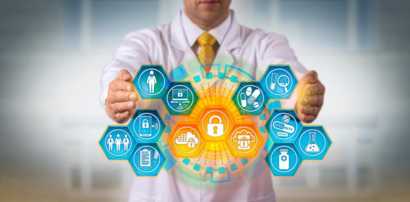A business professional in a white shirt and yellow tie holds his hands protectively around a glowing digital security network displaying various cybersecurity icons including locks, shields, and data protection symbols arranged in hexagonal formations.